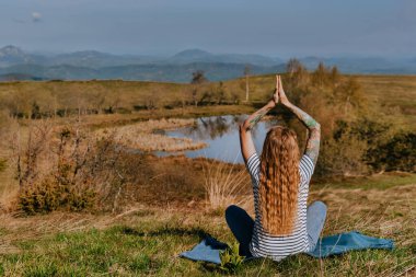 Sırbistan 'ın Golija Dağı' ndaki Nebeska Suza Gölü veya Tear of Haven yakınlarındaki bir tepede tek başına meditasyon yapan dövmeli kadın. Kadın yalnız gezgin, sabah yogası yapıyor, sessizliğin ve yalnız kalmanın tadını çıkarıyor..