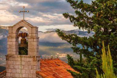 Gün batımında dağlardaki tepedeki eski taş kilise. Tepedeki küçük Ortodoks Hıristiyan kilisesine yakın akşam manzarası, altın güneş ışığı ve perde arkasındaki dramatik bulutlar.