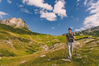 Sırt çantasıyla yürüyen bir adam ve yaz günü kayalık dağ yolunda yürüyüş direkleri. Genç erkek turist manzaranın tadını çıkarıyor, tek başına dışarı çıkıyor. Hafta sonu yürüyüş için aktif sağlıklı yaşam tarzı.