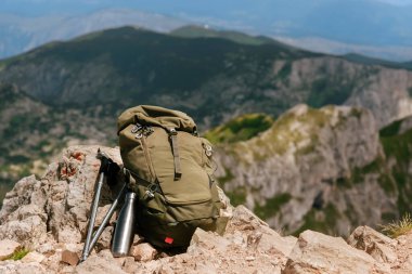 Sırt çantası, metal su şişesi ve dağın tepesinde yürüyüş direkleri. Kayalık kayalıklarda taşa dayanan turizm ekipmanları. Seyahat yaşam tarzı, macera tatili, dağ yürüyüşü konsepti.