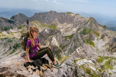 Bobotov kuk dağının tepesinde sırt çantalı, köpekle oturan dövmeli kadın turist. Genç bayan yürüyüşçü köpeğiyle dışarıda güzel vakit geçirmekten hoşlanır. Aktif seyahat yaşam tarzı, evcil hayvan macerası ve yürüyüş konsepti.