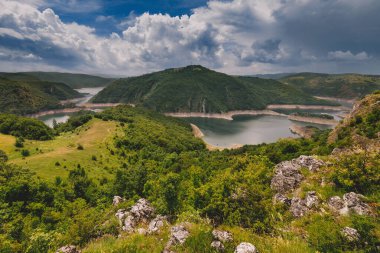 Dağlar arasında Uvac Nehri 'nin dolaştığı dağ manzarası ve dramatik yağmur bulutları altında yeşil ağaçlık tepeler. Sırbistan 'daki Uvac Özel Doğa Rezervindeki Panorama. Balkanlar 'ın doğasını keşfetmek.