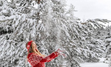 Sıcak süveter giyen, saç bandı ören ve beyaz orman arka planında karla oynayan genç kadınlar. Karlı ağaçların arasında duran dişi ilk karın tadını çıkarıyor. Mutlu kış ve Noel tatilleri.