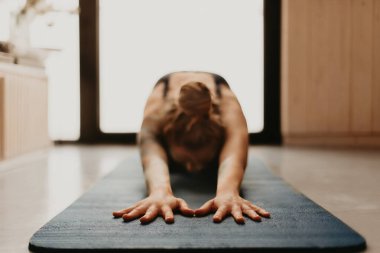 Evde yoga yapan, antrenmandan sonra dinlenen, paspasa dokunmaya odaklanan bir kadın. Kadın evde ya da modern stüdyoda çocuk pozu veriyor. Rahatlama, esneme ve meditasyon konsepti.