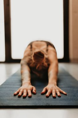 Evde yoga yapan, antrenmandan sonra dinlenen, paspasa dokunmaya odaklanan bir kadın. Kadın evde çocuk pozu veriyor. Rahatlama, esneme ve meditasyon konsepti.