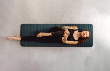 Kadının esneme egzersizi yaptığını, yoga yaptığını, spor minderinde uzandığını, dizlerini büktüğünü ve göğsüne geldiğini görmek. Kadın, evde, yoga stüdyosunda ya da spor salonunda rüzgâr serbest bırakma pozu veriyor..