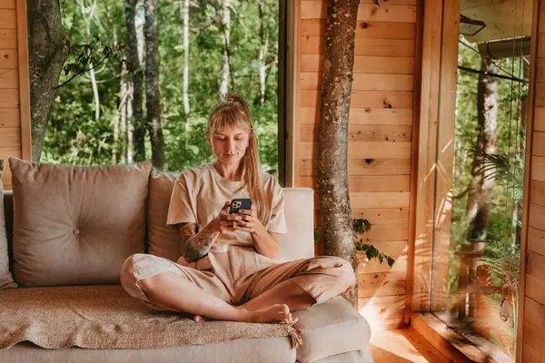 Akıllı telefon tutan, tatilde internete mesaj atan ya da sörf yapan bir kadın. Kadın rahat bir ağaç evde kanepede dinleniyor, mesajları okuyor ve kontrol ediyor ya da cep telefonunda uygulama kullanıyor..