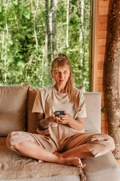 Kadınlar tatil boyunca ahşap kulübede akıllı telefonlarıyla bağlı kalırlar. Kadın rahat bir ağaç evde kanepeye uzanıp mesajları okuyor ve kontrol ediyor ya da akıllı telefonlarda uygulama kullanıyor..