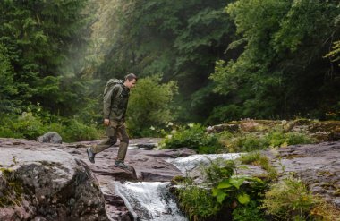 Arbinje nehir vadisinde sisli bir sis ile uyanan turist sırt çantalı erkek yürüyüşçü. Sırt çantası gezisi sırasında yürüyüş rotasında kayalık sularda gezinen maceraperest adam..