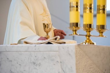 interiors and details in catholic church view of the altar, candles, priest and the chalice