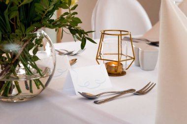 tableware and table decorations at celebrations place cards on a white tablecloth with cutlery and candle