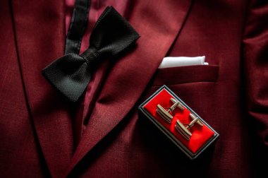 bride and groom's wardrobe and items of clothing bow tie, cufflinks and pocket square lying on a maroon jacket