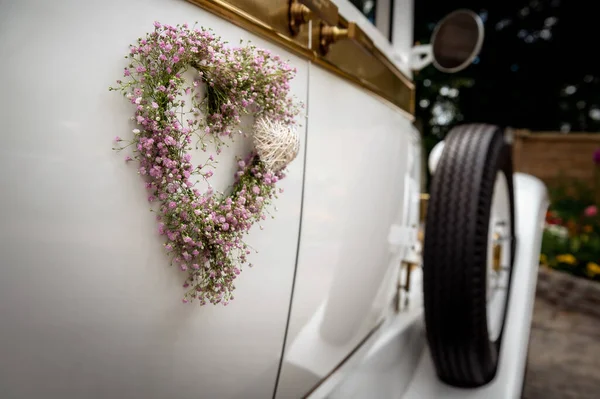 decorations and details on a wedding car heart of tiny pink flowers on the side of a white vintage car