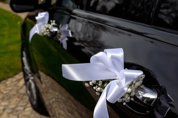 decorations and details on the wedding car white ribbon and tiny flowers on the door handle of a black modern car small depth of field