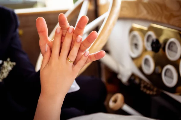 decorations and details on the car for the wedding intertwined hands of the bride and groom inside a white vintage car with a wooden steering wheel in the background