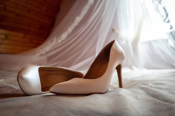 bride and groom's wardrobe and items of clothing bride's high heel shoes lying on the bed against the background of a blurred white veil