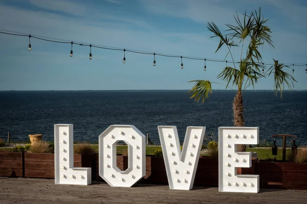 wedding hall interiors and decorations illuminated love inscription against the background of wooden pots, palm trees and the blue sea