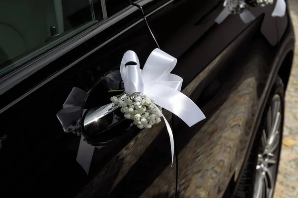 decorations and details on the wedding car white ribbon and tiny flowers on the door handle of a black modern car small depth of field
