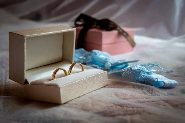wedding rings and details a white box with wedding rings and a blue garter lying on the bed against the backdrop of a white veil