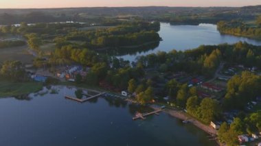 Yaz öğleden sonra Polonya 'daki Kashubian köyü ve göllerinin hava manzarası. Altın saat, kamp, tekneler ve gölde iskele. Geri uçuş çekimi.