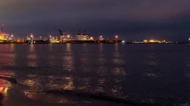 Akşamları çalışan bir Polonya konteynır limanında zaman kaybı. Dalgalanan su, ışıkların yansımaları ve gökyüzündeki bulutların akışı..