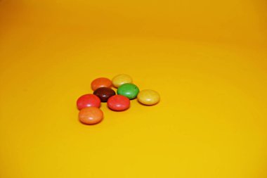 Renkli şekerlerle kaplı çikolata topları. Sarı arka planda izole edilmiş renkli çikolata şekeri.