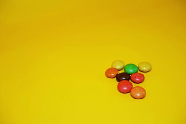 Renkli şekerlerle kaplı çikolata topları. Sarı arka planda izole edilmiş renkli çikolata şekeri.
