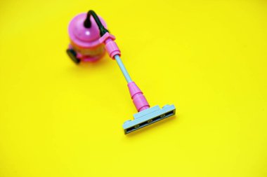 Plastik bloklardan yapılmış mini elektrikli süpürge oyuncağı. Sarı arkaplanda izole edilmiş elektrikli süpürge oyuncağı.