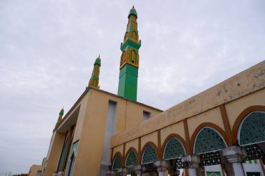 Yeşil ve sarı karışımlı cami kulesi. Bulutlu bir gökyüzü arka planına karşı cami minaresi