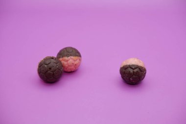 Üç çikolatalı top, yarı kahverengi ve yarı pembe. Mor arka planda izole edilmiş çikolata topu atıştırmalığı. Çikolatalı çerez futbol topuna benziyor..