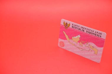 Endonezyalı çocuk kimlik kartı, parlak kırmızı bir arka plana yerleştirilmiş. Kartın arkası açıkça görülüyor, tasarımını ve detaylarını gösteriyor..