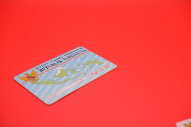 Endonezya kimlik kartı parlak kırmızı bir arka plana yerleştirilmiş. Kartın arkası açıkça görülüyor, tasarımını ve detaylarını gösteriyor..