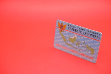 Endonezya kimlik kartı parlak kırmızı bir arka plana yerleştirilmiş. Kartın arkası açıkça görülüyor, tasarımını ve detaylarını gösteriyor..