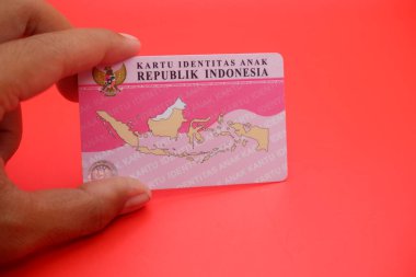 Endonezyalı çocuk kimlik kartı, parlak kırmızı bir arka plana yerleştirilmiş. Kartın arkası açıkça görülüyor, tasarımını ve detaylarını gösteriyor..