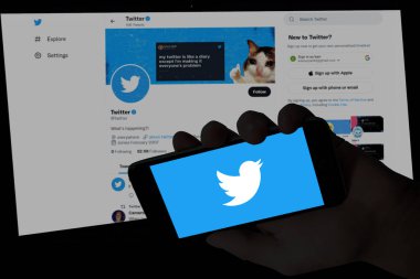 Twitter logosuyla el ele tutuşan ve arka planda bulanık bilgisayar ekranı görüntülenen twitter web sitesi. Resimli başyazı.