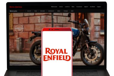 Royal Enfield şirketinin logosu mobil olarak sergileniyor ve internet siteleri bilgisayar ekranında bulanıklaşıyor. Resimli başyazı.