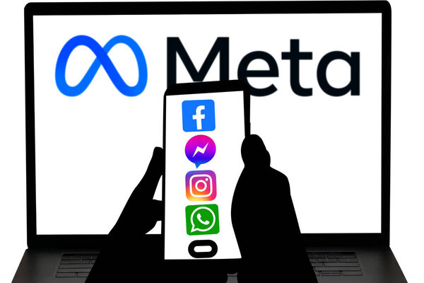 Meta company apps logo in mobile screen and meta company logo displayed in blurred computer screen. This company owns Facebook, Instagram, and WhatsApp and more.