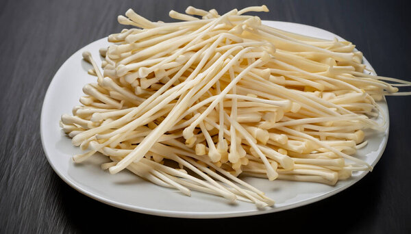 lot of Enoki mushroom in white plate. isolated on dark background. selective focus.