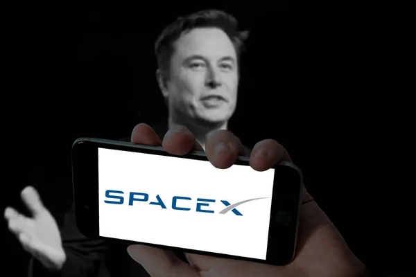 Cep telefonunda SpaceX logosu ve bulanık arkaplanda Elon misk resmi.
