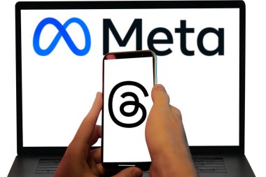 Threads Instagram app logo in holding mobile and Meta logo in laptop screen background.