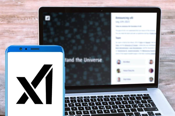  xAI logo in holding mobile screen and xAI website page in blurred laptop screen background.