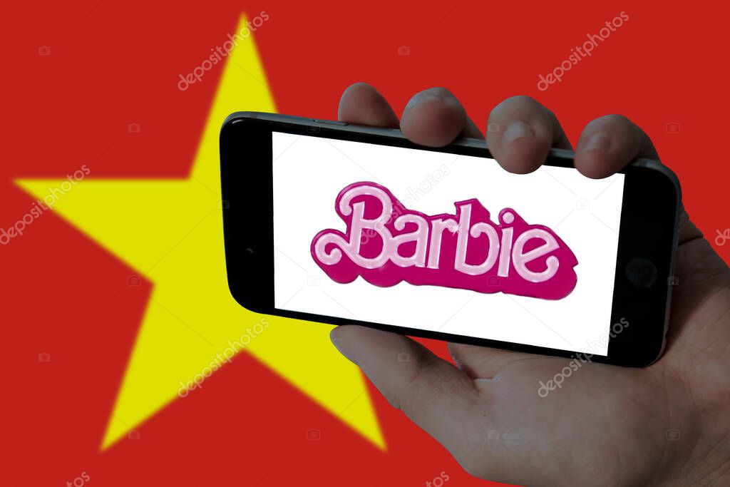 Barbie movie logo in holding mobile screen and blurred Vietnam flag in background