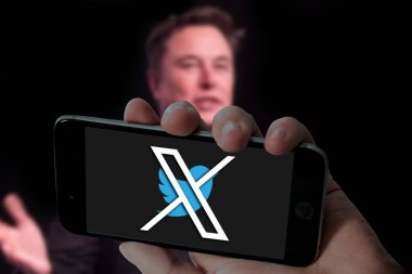 Cep telefonunda kuş logosu olan Twitter X ve bulanık dizüstü bilgisayar arka planında Elon misk resmi.