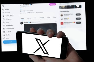 Cep telefonunda Twitter X logosu ve bulanık dizüstü bilgisayar ekranı arka planında Elon misk twitter sayfası 
