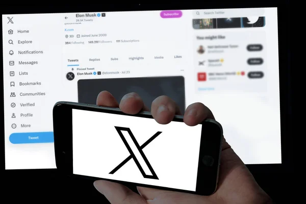 Cep telefonunda Twitter X logosu ve bulanık dizüstü bilgisayar ekranı arka planında Elon misk twitter sayfası 