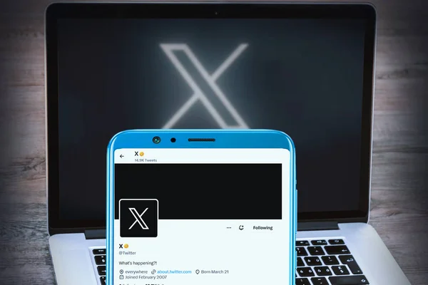 Mobil ekranda Elon misk twitter sayfası ve bulanık dizüstü bilgisayar arka planında X logosu.
