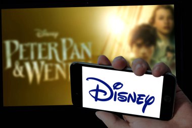 Cep telefonunda Disney logosu ve bulanık dizüstü bilgisayar arka planında Peter Pan ve Wendy filmi