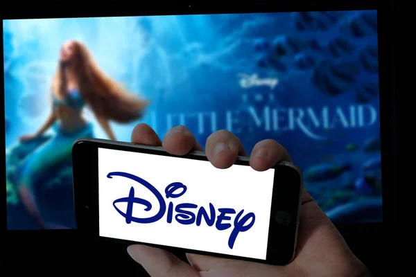 Cep telefonundaki Disney logosu ve bulanık dizüstü bilgisayarın arka planındaki küçük deniz kızı filmi.