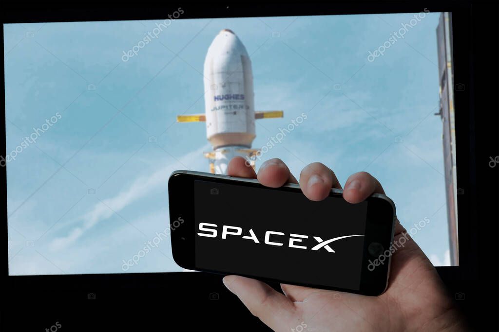 SpaceX logo in holding mobile screen and Hughes Jupiter 3 launch in blur computer screen background.