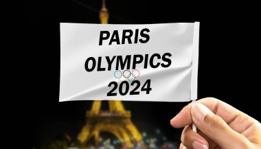 Paris Olimpiyatları 'nın 2024 metni Eiffel kulesinin bulanık arka planında izole edilmiş bayrak tutarken görülüyor.